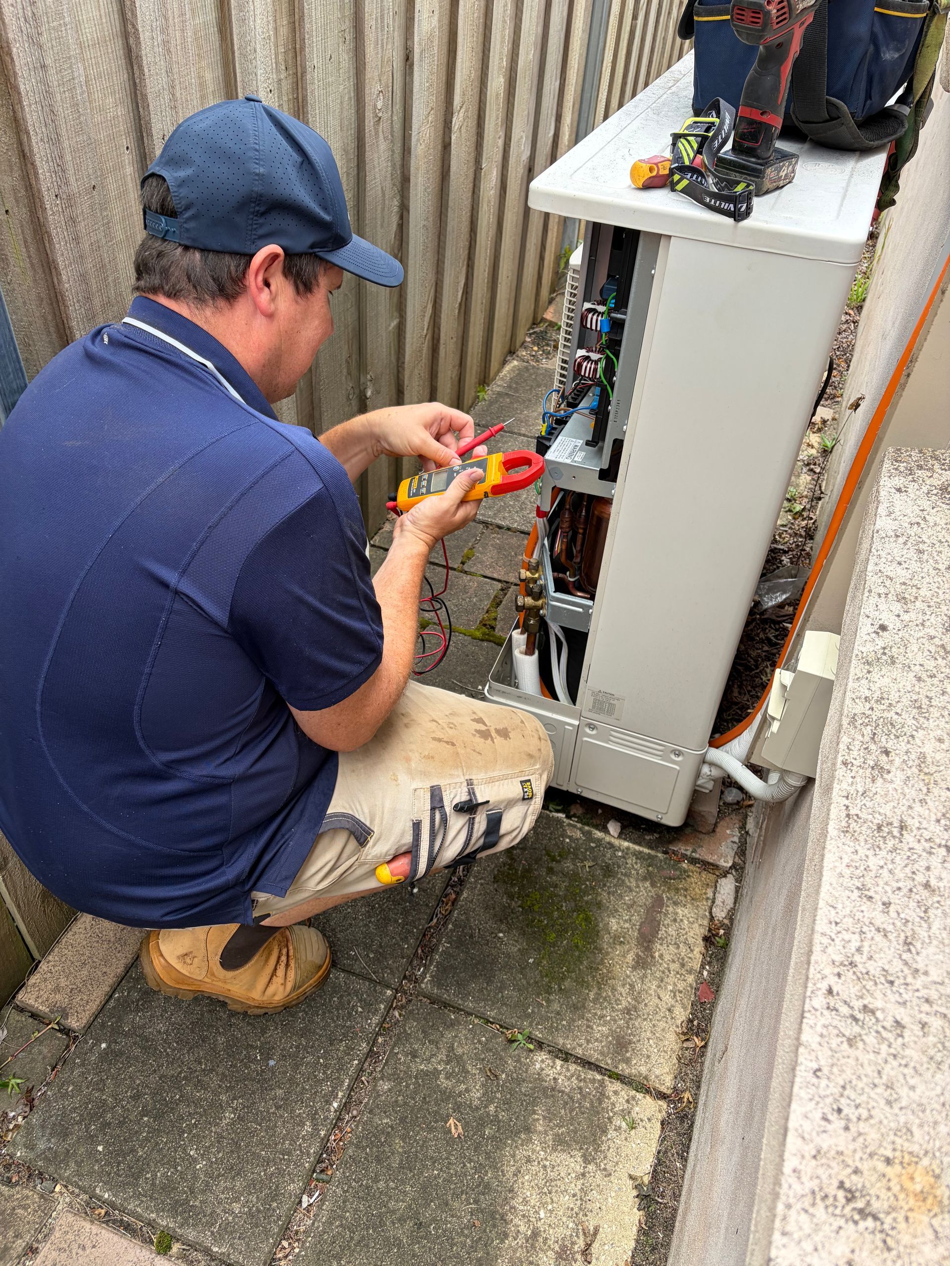 Technician kneeling by an outdoor electrical cabinet, using tools to repair wiring — Escarpment Air in Shellharbour, NSW