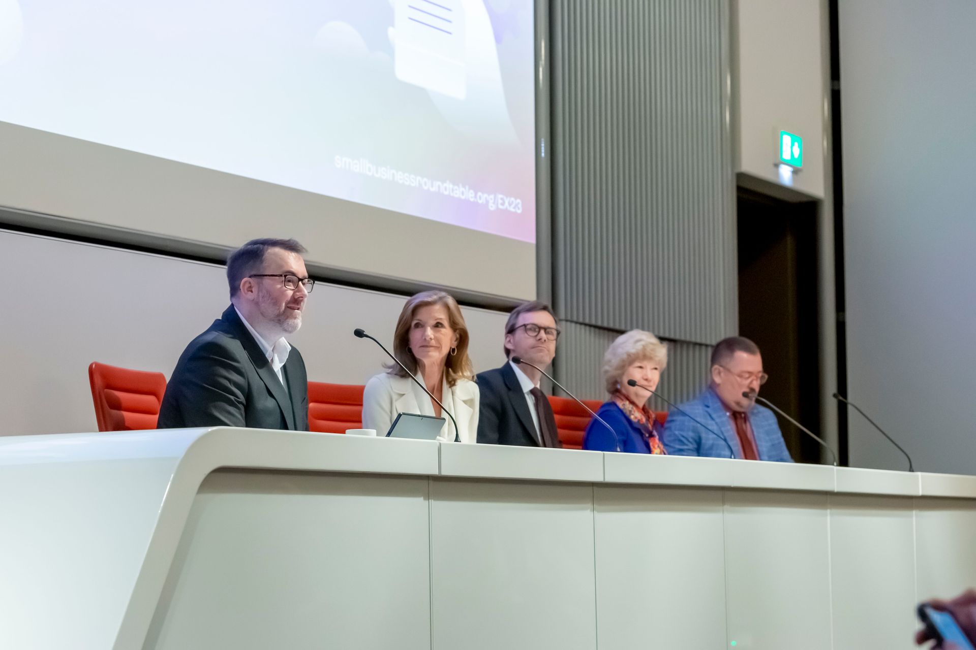 A group of people are sitting at a table in front of microphones in a conference room.