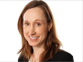 A woman with long brown hair is smiling and wearing a black jacket.