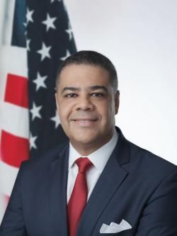 A man in a suit and tie is standing in front of an american flag