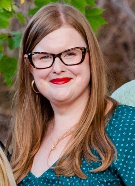 A woman wearing glasses and red lipstick is smiling for the camera.