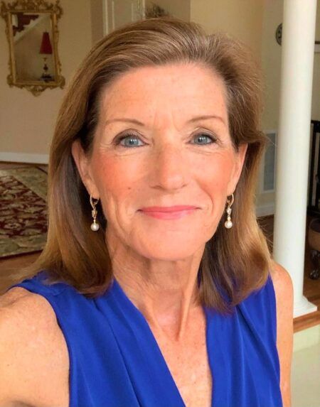 A woman wearing a blue top and pearl earrings smiles for the camera