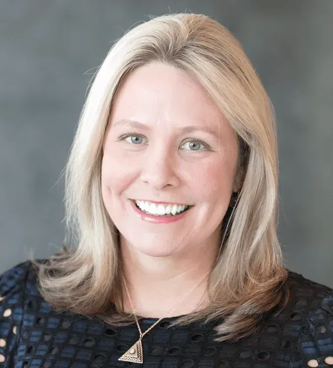 A woman wearing a black shirt and a necklace is smiling for the camera.