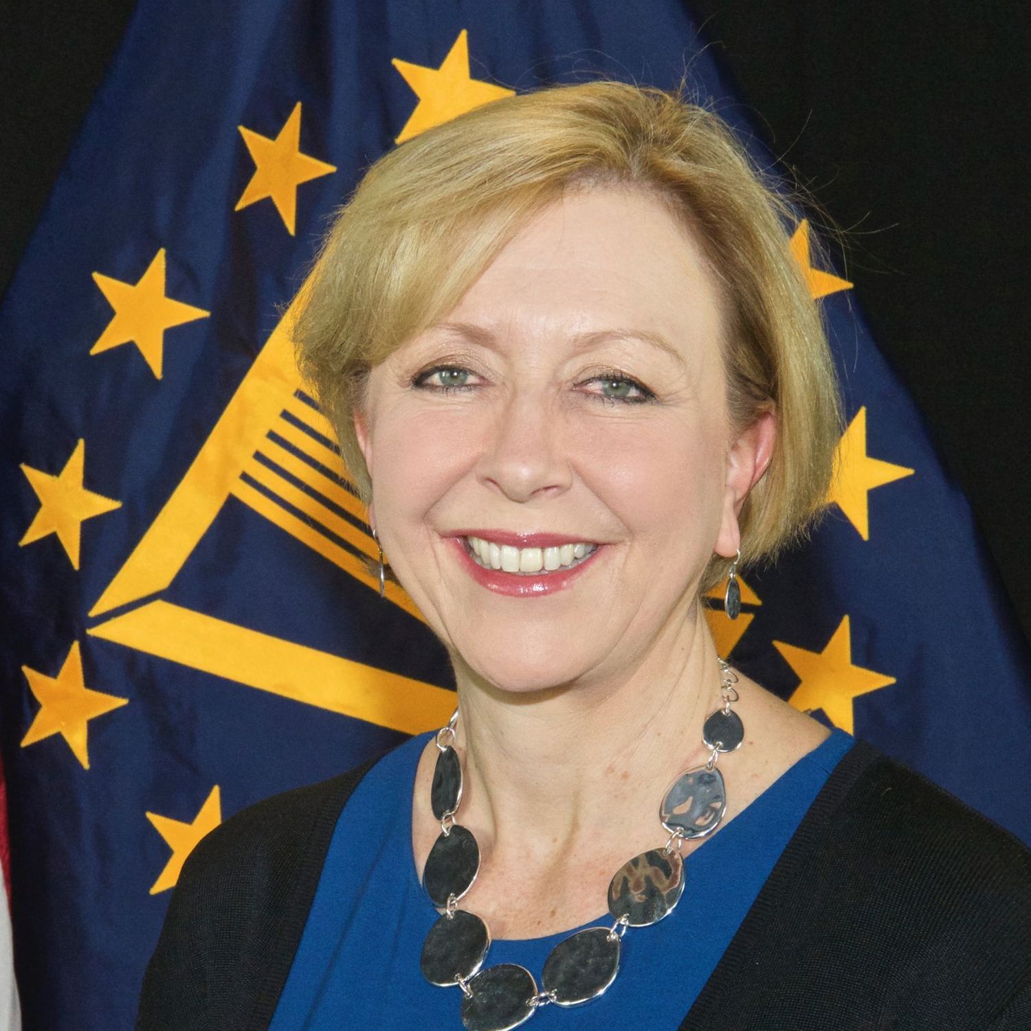 A woman is smiling in front of an american flag