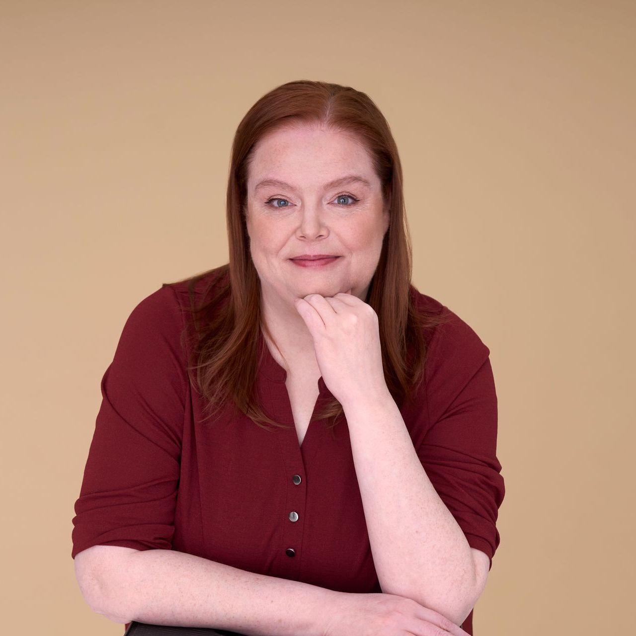 A woman in a red shirt is smiling with her hand on her chin