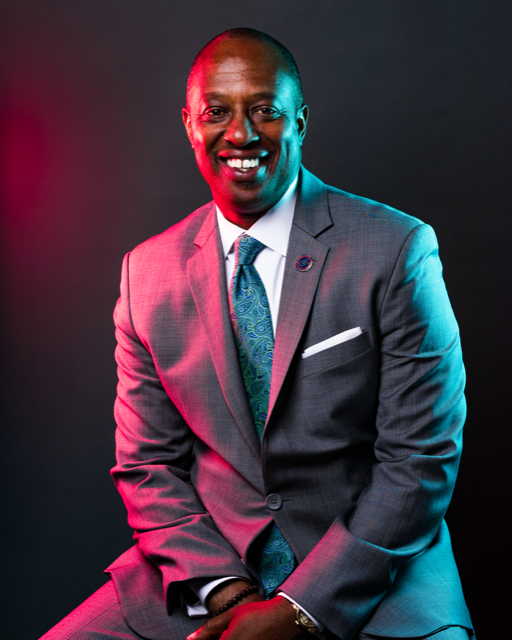 A man in a suit and tie is sitting down and smiling.