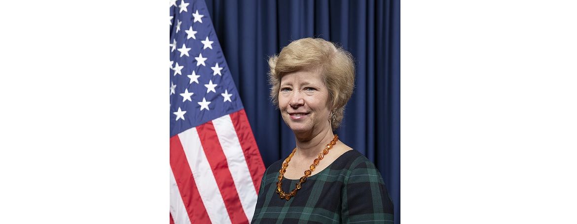A woman is standing in front of an american flag.
