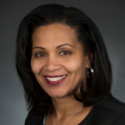A woman wearing a black jacket and earrings smiles for the camera