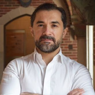 A man with a beard wearing a white shirt with his arms crossed