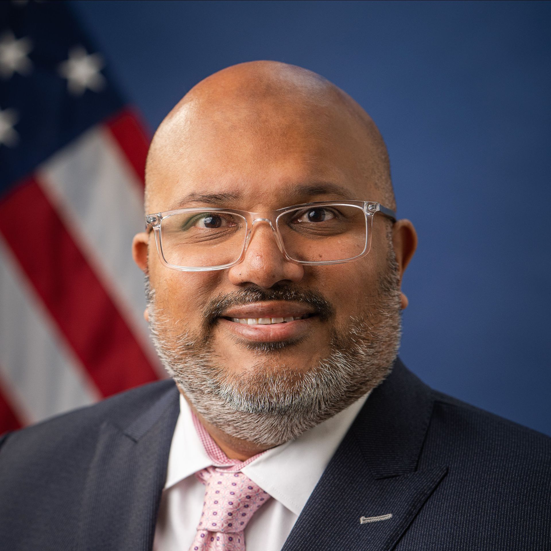A man in a suit and tie is smiling in front of an american flag.