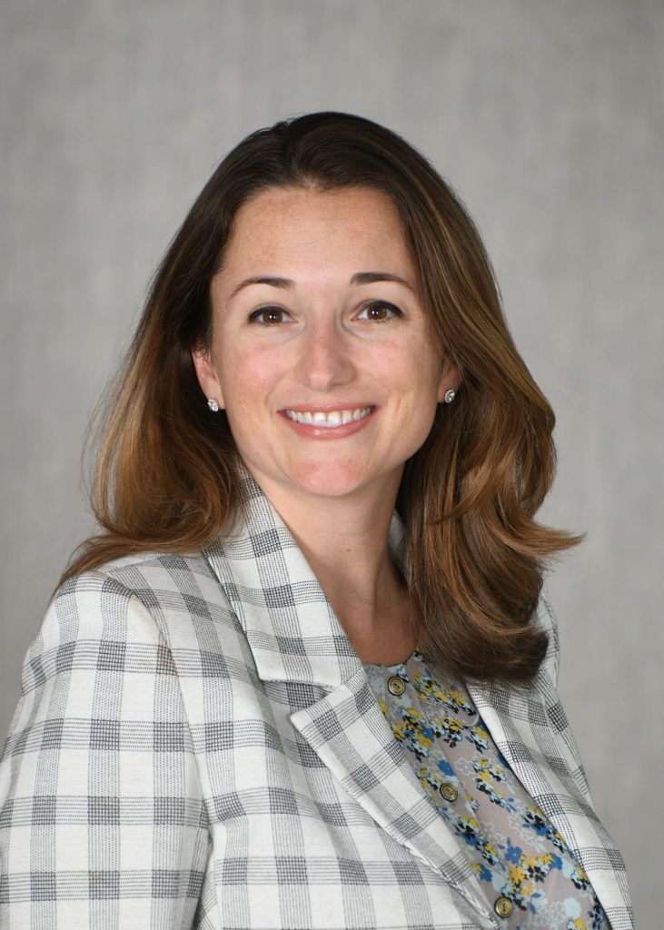 A woman in a plaid jacket and floral shirt is smiling for the camera.