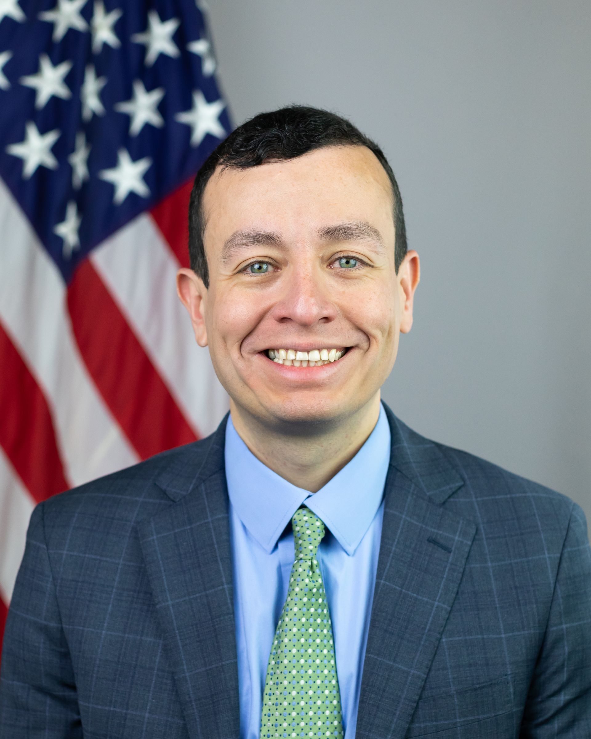 A man in a suit and tie is smiling in front of an american flag.