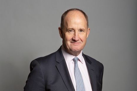 A man in a suit and tie is standing in front of a gray background.