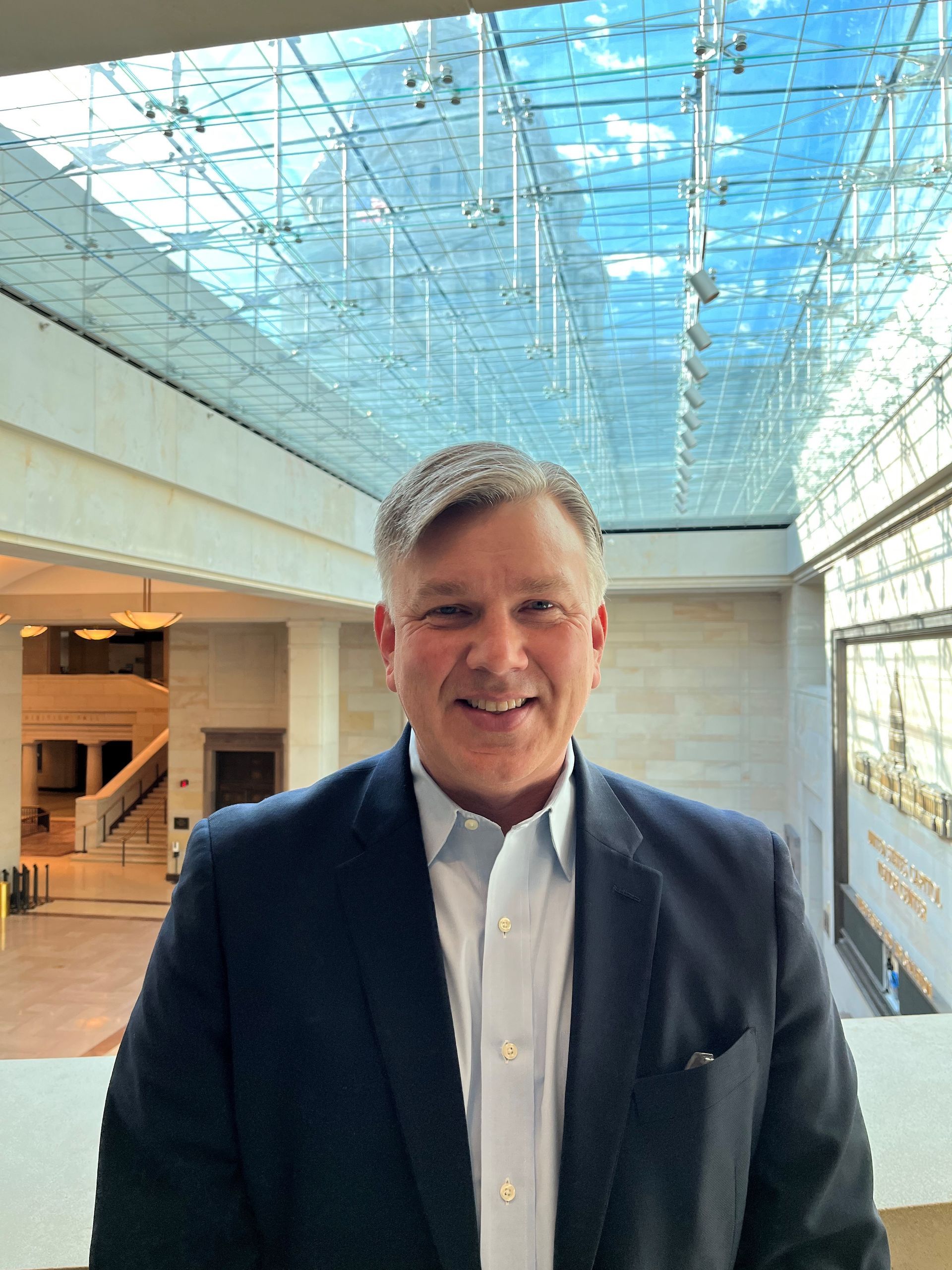 A man in a suit and white shirt is standing in front of a glass ceiling.