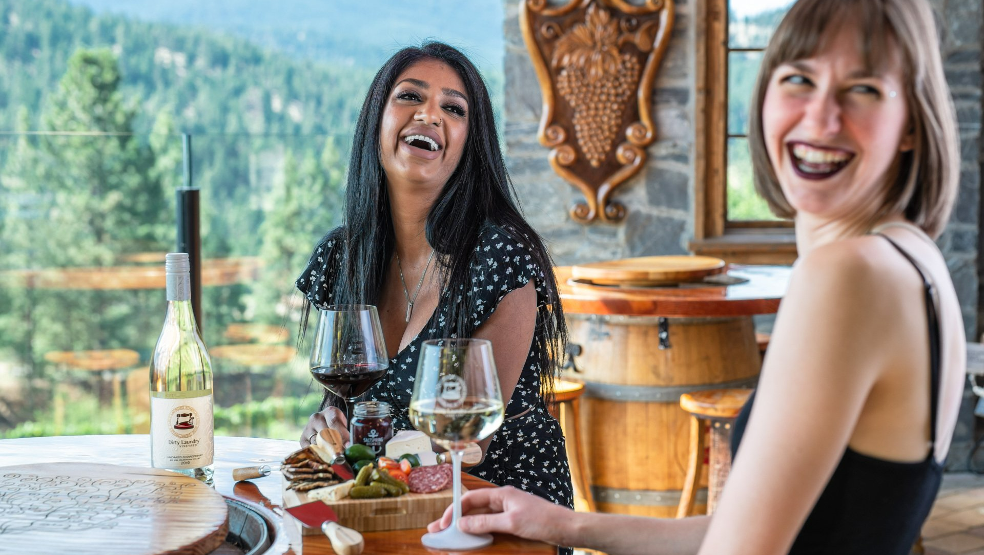 Two women are sitting at a table drinking wine and laughing.