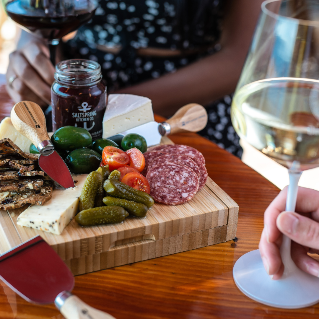 A person is holding a glass of wine next to a cutting board with food on it