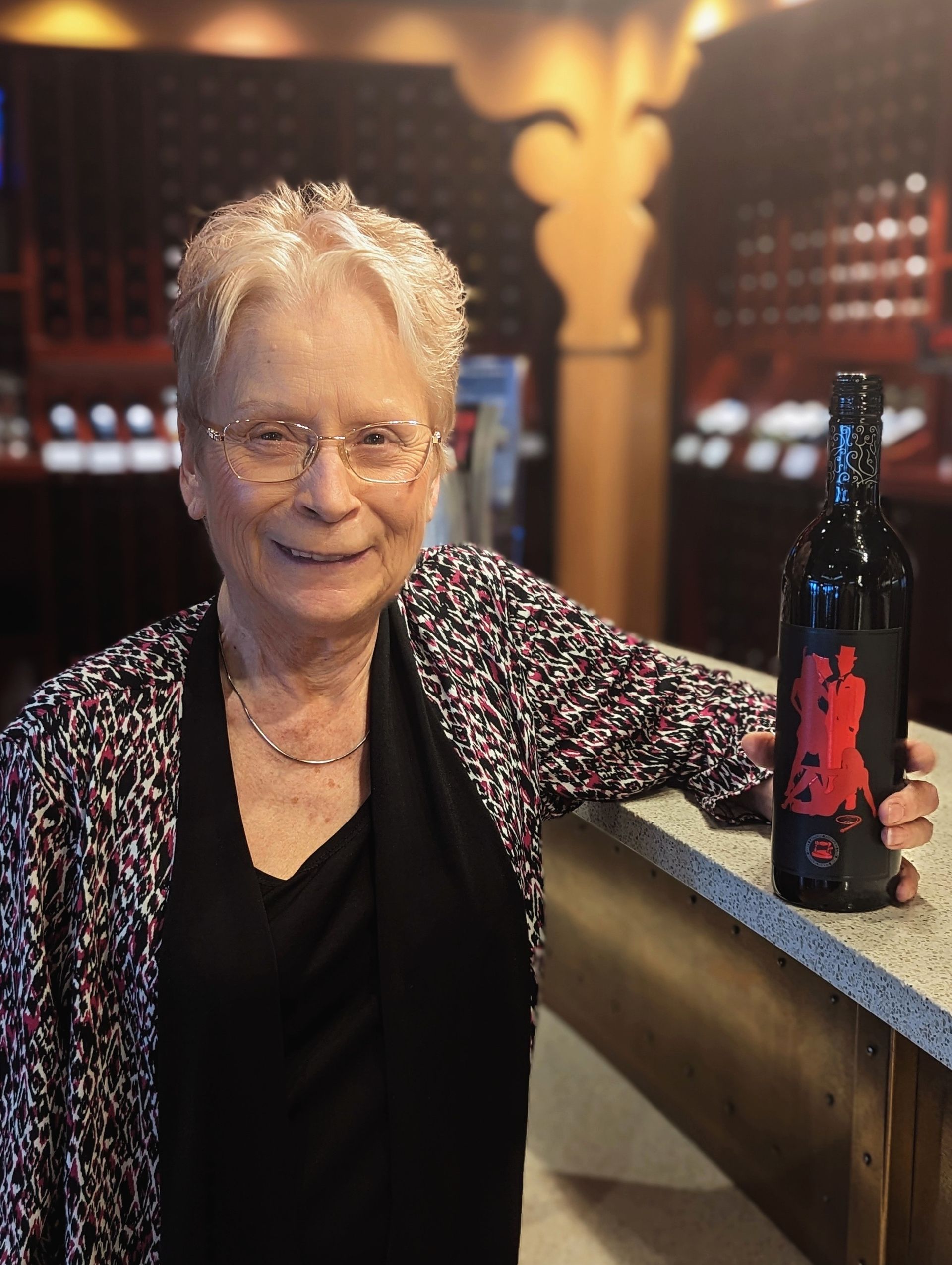 An elderly woman is holding a bottle of wine