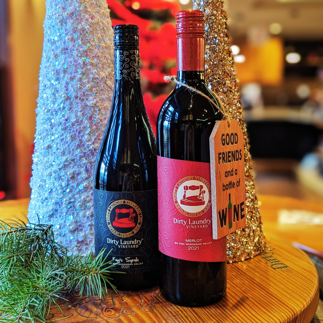 Two bottles of wine are sitting on a wooden table next to a christmas tree.