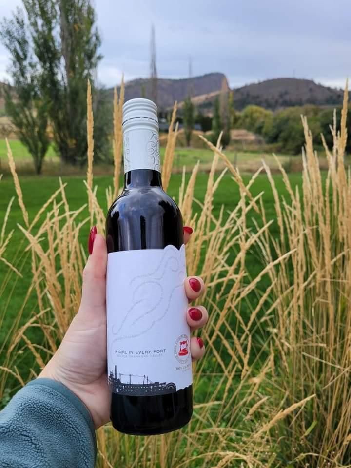 A person is holding a bottle of wine in front of tall grass.
