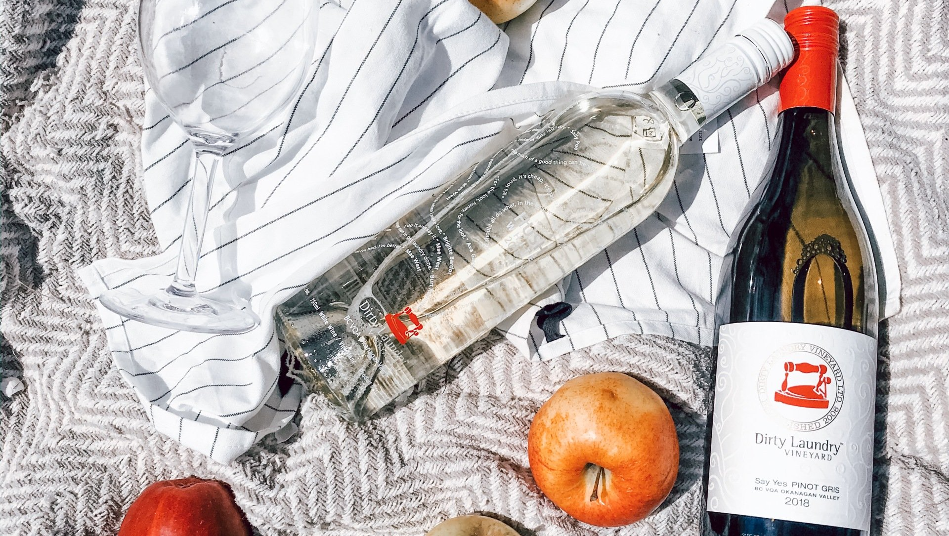 A bottle of wine is sitting on a picnic blanket next to apples.