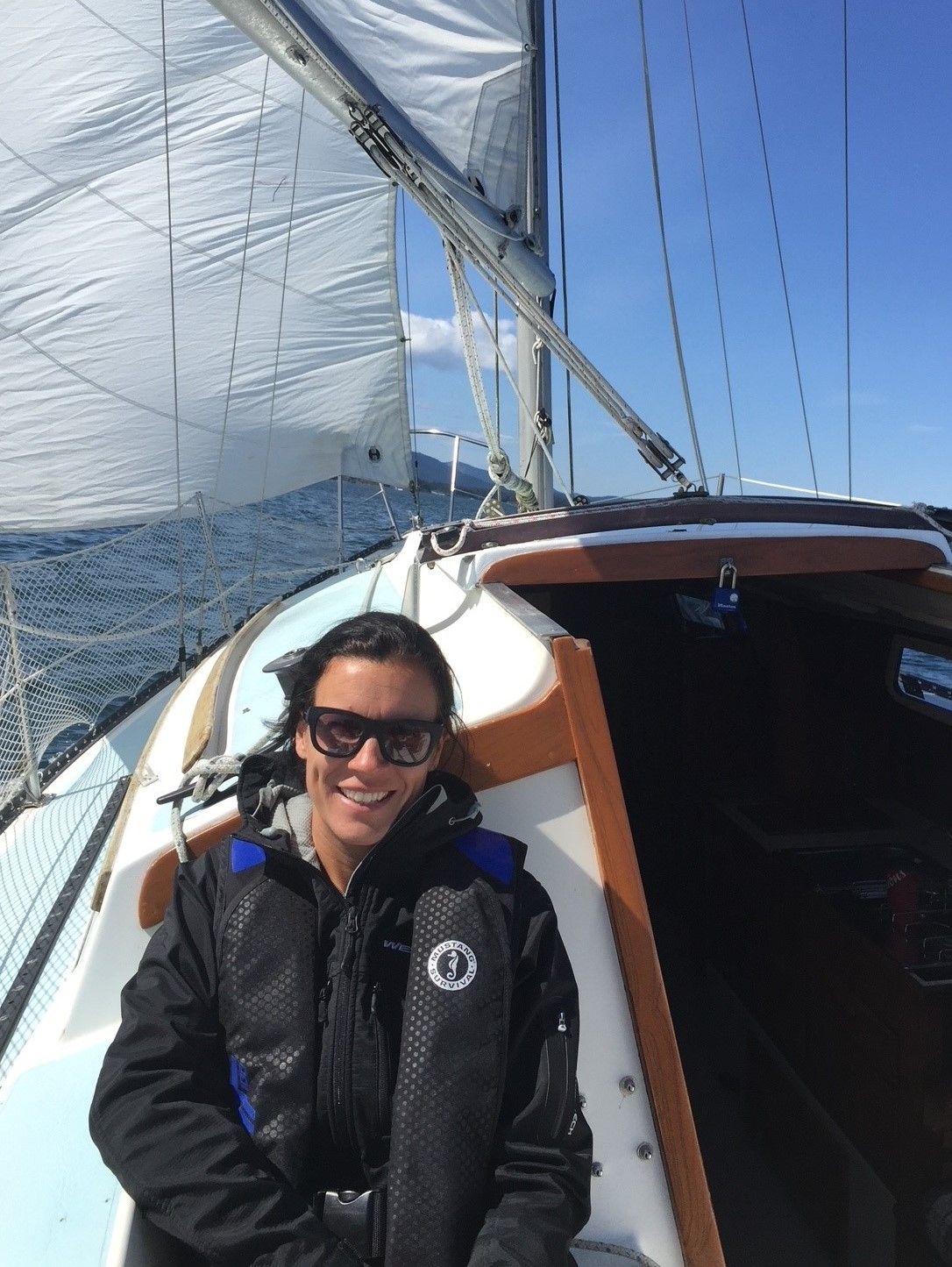 A man wearing sunglasses and a life jacket is sitting on a sailboat.