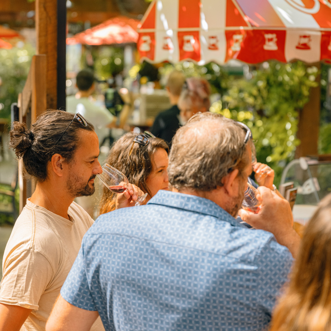 A group of people are drinking wine under an umbrella.