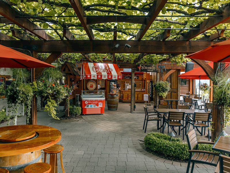 A restaurant with tables , chairs and umbrellas under a pergola.