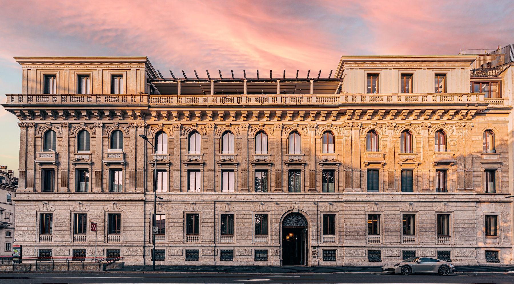 A large, stone building in Rome with many windows and a cloudy sunset sky above.