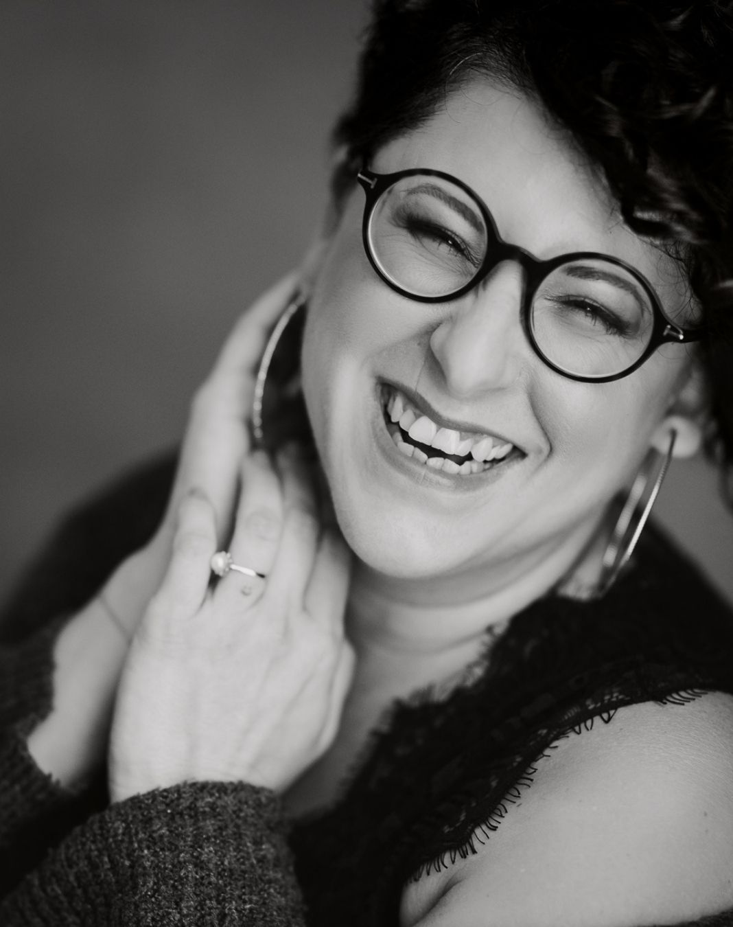 Eine Frau mit Brille und Ohrringen lächelt auf einem Schwarzweissfoto.