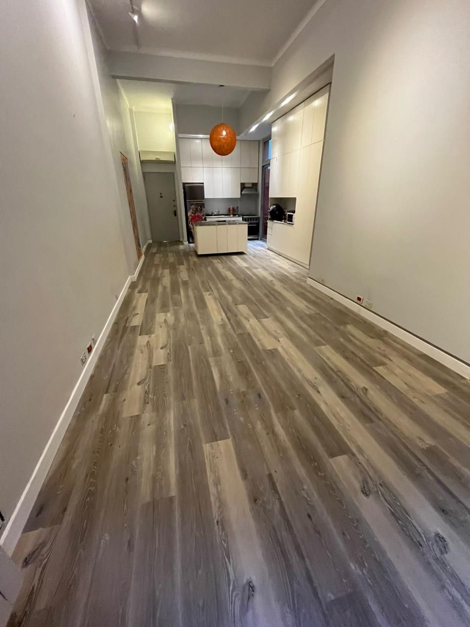 Persona instalando suelo de madera en un luminoso salón con un sofá gris y una mesa de centro de cristal.
