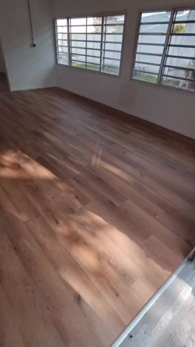 Habitación vacía con suelo de madera y grandes ventanales que dejan entrar la luz natural.