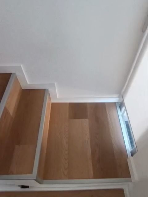 Escaleras de madera y rellano en un pasillo blanco, vistas desde arriba.
