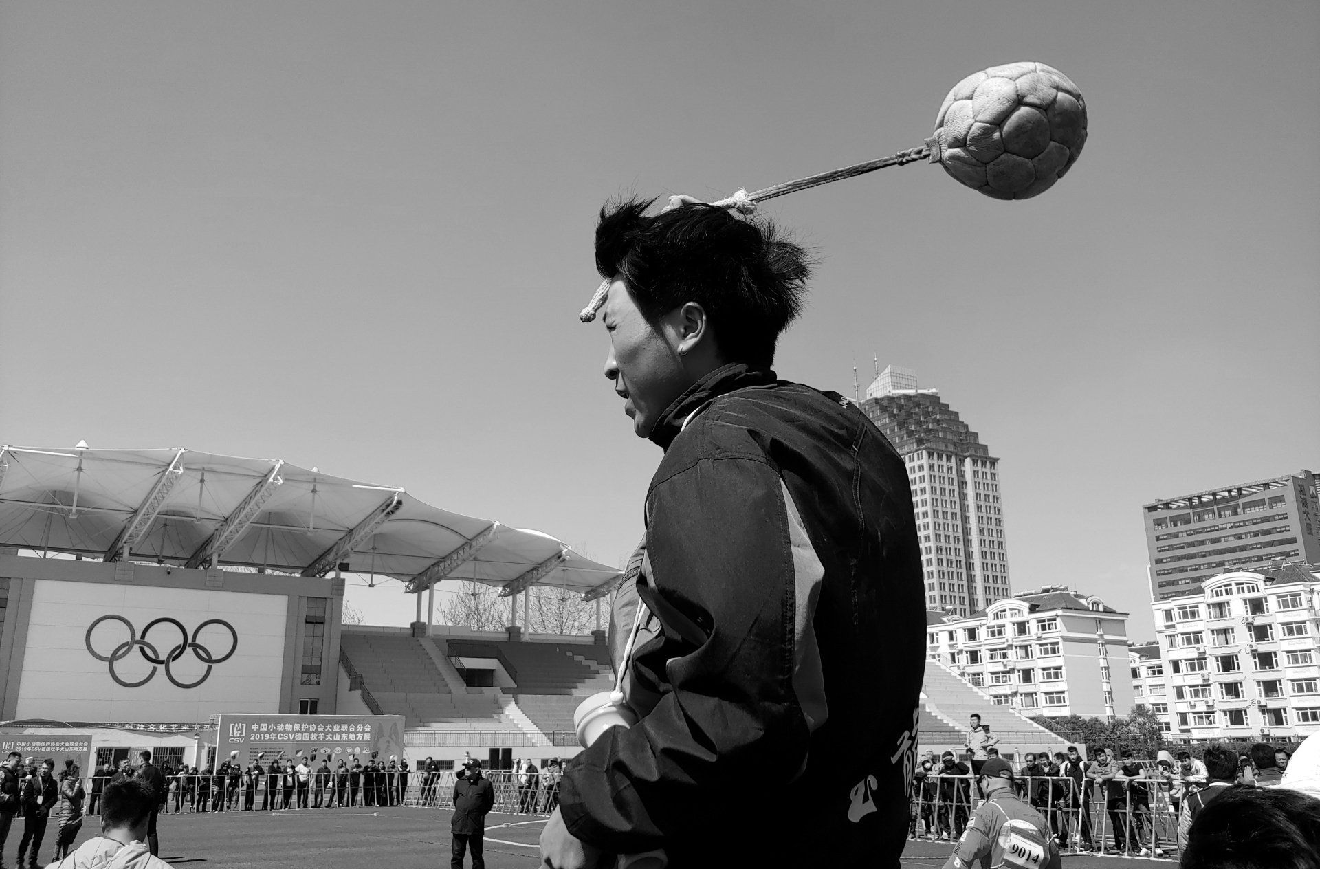 Un homme tient un ballon de football sur sa tête devant un panneau olympique