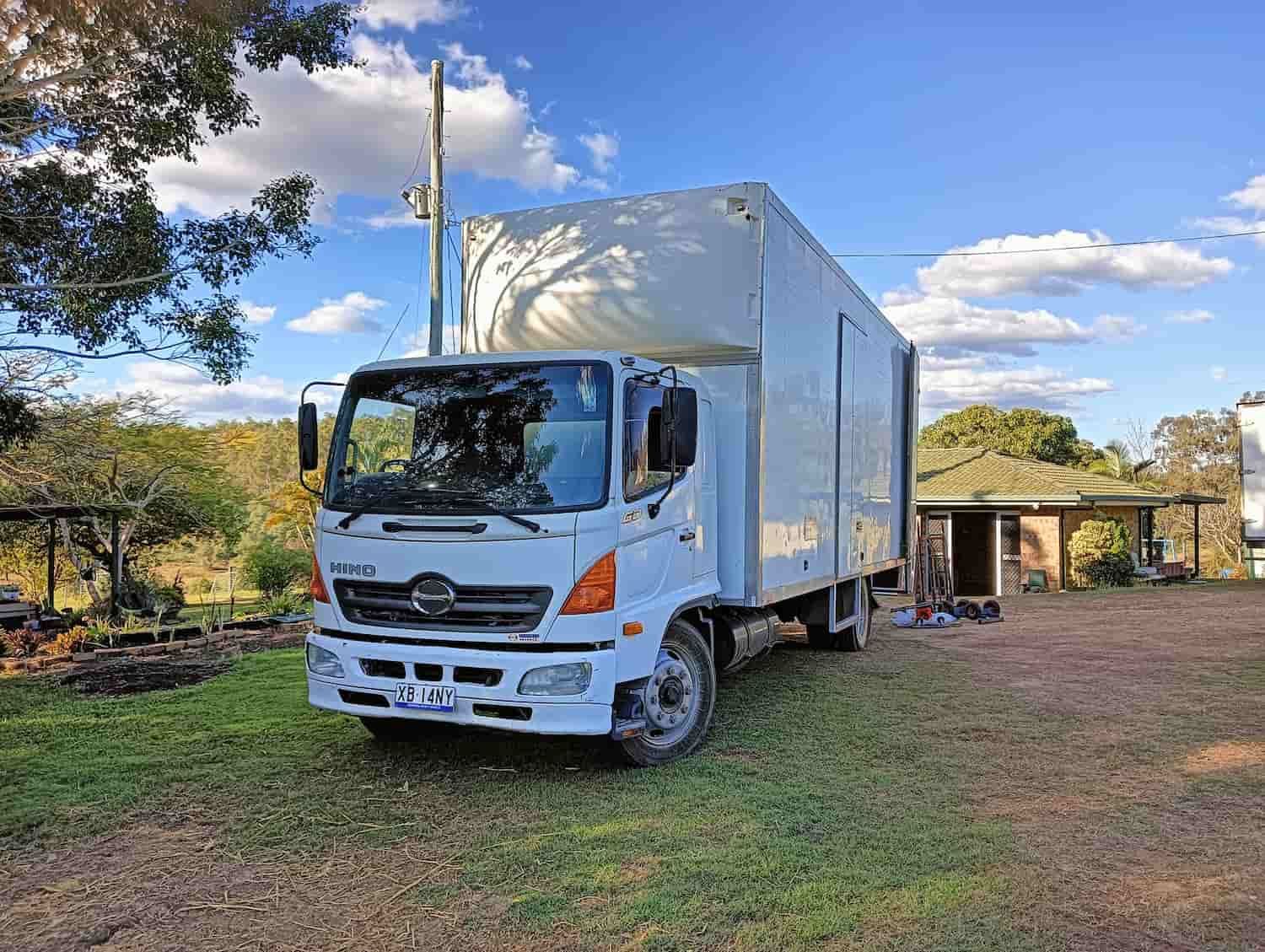 a White Truck is Parked in a Grassy Field in Front of a House — CM Removals & Transport In Gympie, QLD
