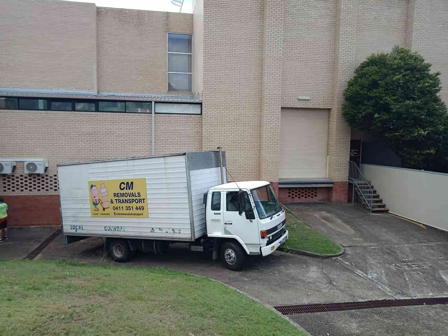 a White Moving Truck is Parked in Front of a Brick Building — CM Removals & Transport In Gympie, QLD