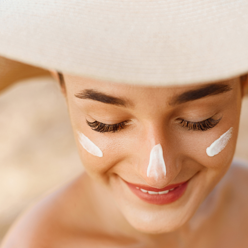 Eine Frau mit Hut hat Sonnencreme im Gesicht.