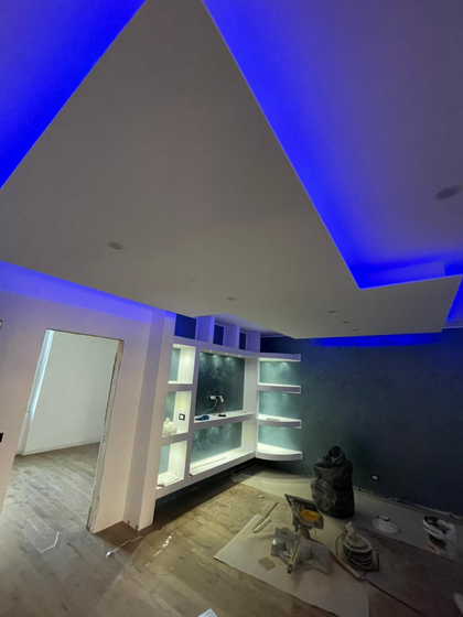 Soggiorno moderno in fase di ristrutturazione, con luci LED blu sul soffitto e scaffali a incasso