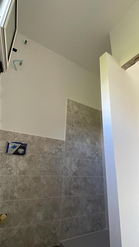 Zona doccia piastrellata con pareti bianche e una porta socchiusa.