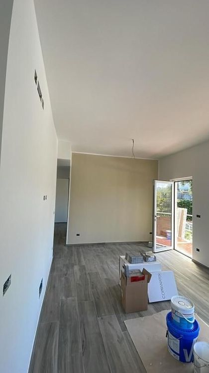 Stanza stretta in ristrutturazione, con pavimento grigio, parete beige, porta a vetri aperta e vernici a terra