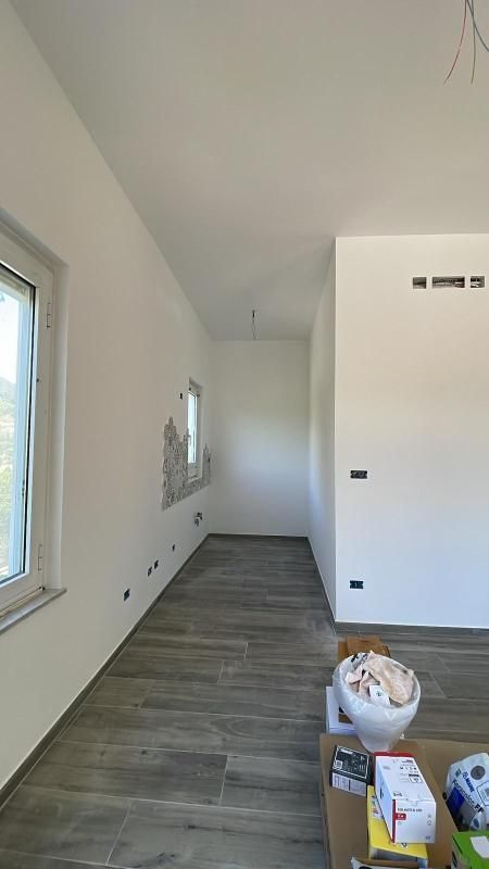 Stretto corridoio bianco con pavimento piastrellato, una finestra e materiali da costruzione sulla destra.