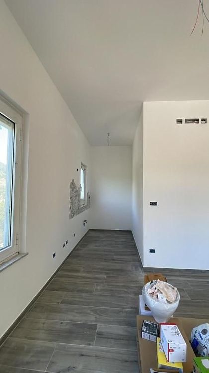 Stretto corridoio bianco con pavimento piastrellato, una finestra e materiali da costruzione sulla destra.