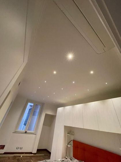 Camera da letto luminosa e minimalista con soffitto spiovente, faretti incassati, finestra e testiera rossa