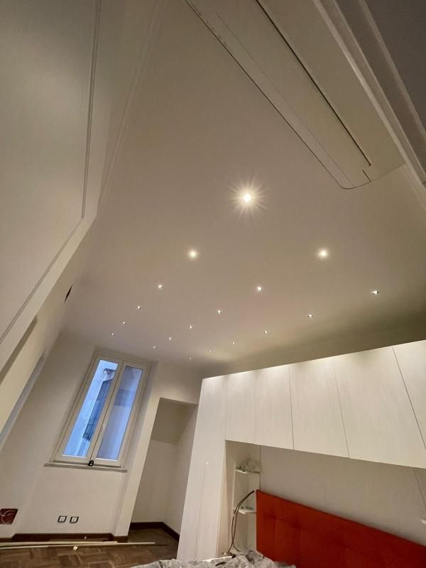 Camera da letto luminosa e minimalista con soffitto spiovente, faretti incassati, finestra e testiera rossa