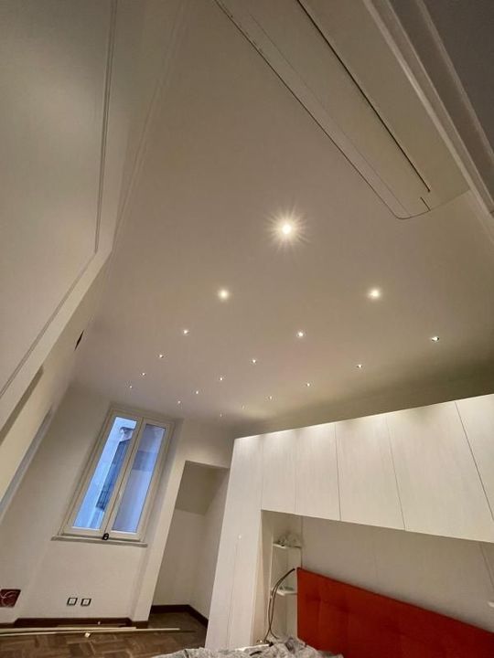 Camera da letto luminosa e minimalista con soffitto spiovente, faretti incassati, finestra e testiera rossa