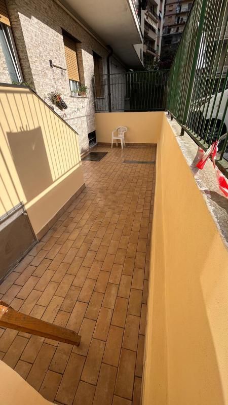 Stretto corridoio esterno lastricato in mattoni accanto a un condominio, con una sedia in fondo e uno stendibiancheria.