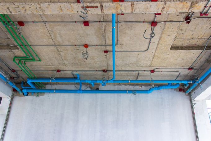 Soffitto con tubi blu e verdi e cavi a vista, sopra una parete bianca in una stanza non finita