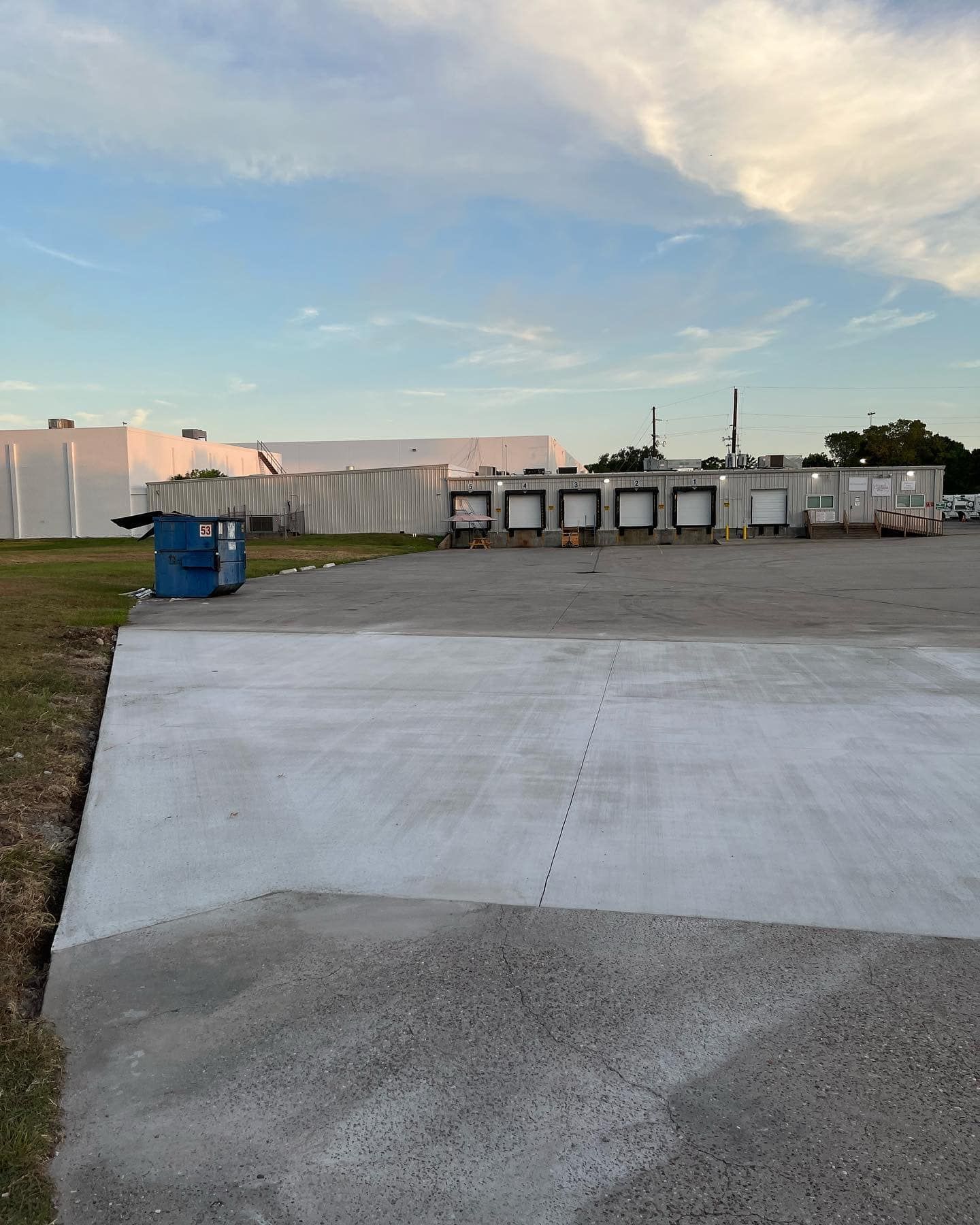 Concrete pad in front of a warehouse with loading docks, blue sky above.
