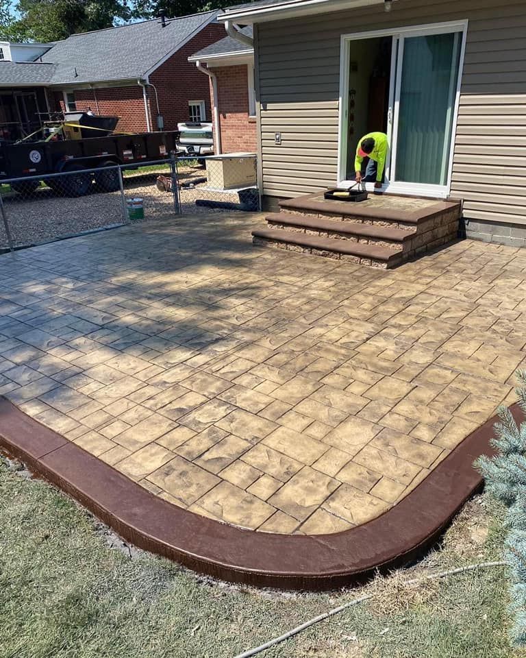 Stamped concrete patio with brown border, steps leading to sliding door, worker in yellow vest.