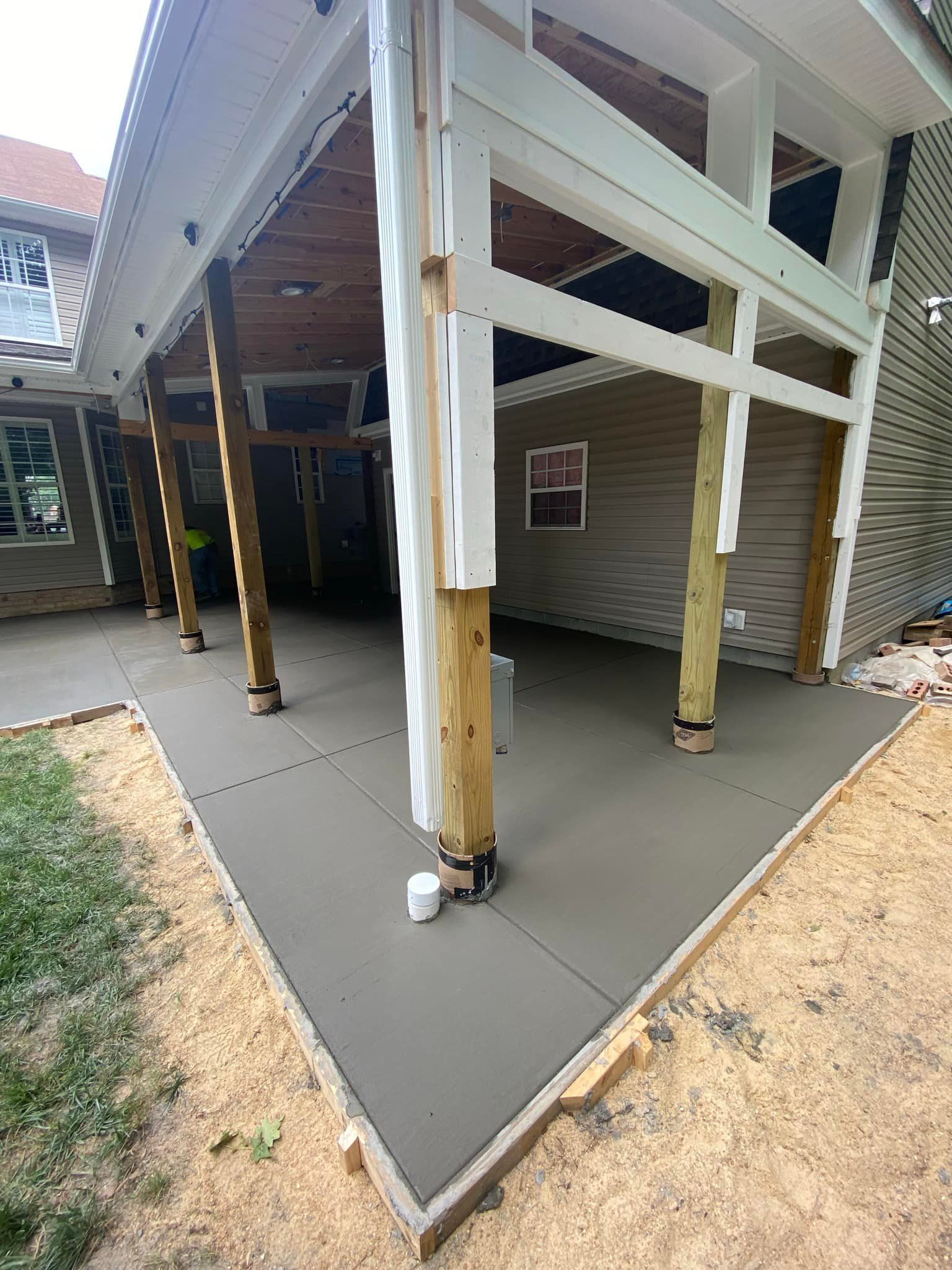 Newly poured concrete patio under a covered porch, wood posts and beams, tan and gray hues.