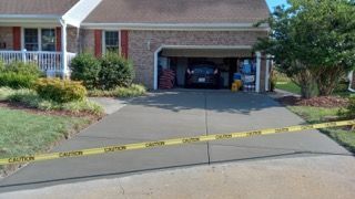 Freshly poured concrete driveway blocked by caution tape in front of a house.